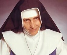 Santa Dulce dos Pobres sorrindo, usando seu hábito azul e branco, segurando as mãos de uma pessoa necessitada