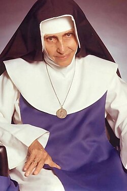 Santa Dulce dos Pobres sorrindo, usando seu hábito azul e branco, segurando as mãos de uma pessoa necessitada