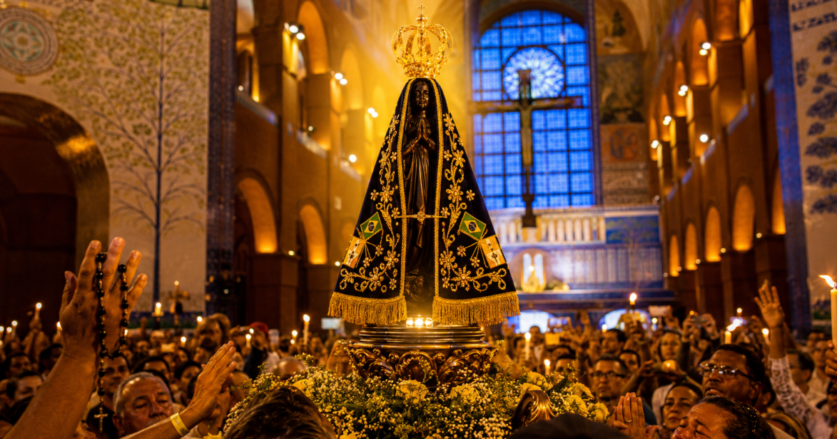 Imagem realista de Nossa Senhora Aparecida iluminada por luz dourada dentro do Santuário Nacional de Aparecida, cercada por fiéis brasileiros em oração, velas acesas e atmosfera espiritual de fé, paz e esperança