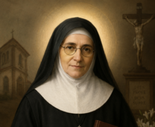 Imagem devocional de Santa Maria Bernarda retratada como uma freira idosa de expressão serena, usando hábito religioso preto e branco, segurando um livro com regras da congregação. Ao fundo aparecem um crucifixo, uma igreja e flores brancas, iluminados por uma suave luz dourada que transmite paz, fé e santidade